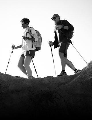 Two people wearing Apple Watch devices and hiking on a rocky trail with poles and gear